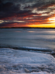 Beautiful sunset over a frozen river with ice cracks. vertical position
