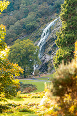 Beautiful shot of green trees and a waterfall descending on green hills on a sunny day