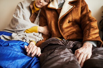 Close up of senior refugee couple hiding in shelter and holding hands in hope during war or crisis,...