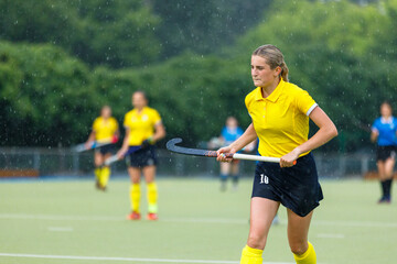 Obraz premium Young teenage girl running on the pitch during the field hockey game in rain