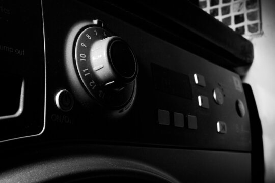 Grayscale shot of the buttons on a washing machine with shadows on it
