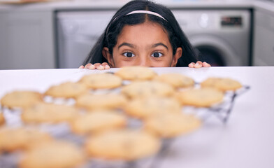 Its just so tempting. Shot of a little girl peeking over the kitchen counter at freshly baked cookies.