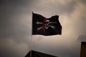 Low angle shot of a waving pirate flag with a skull under storm clouds