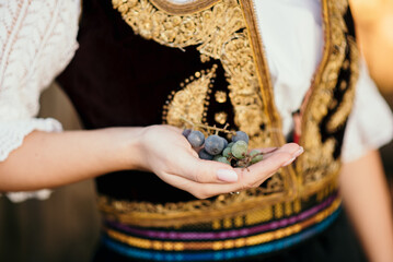 Closeup of golden braid hair  girl in Serbian traditional costume holding grape in her hand