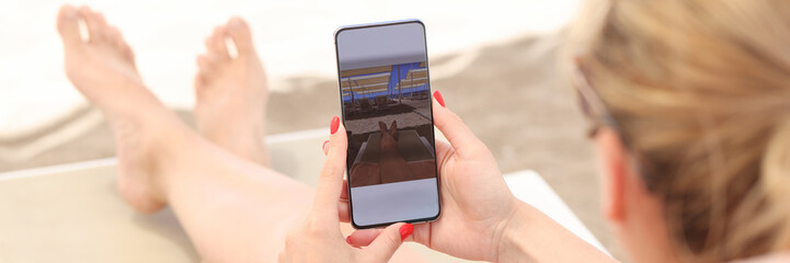 Young woman lying on sun lounger on beach and taking pictures of her feet on mobile phone closeup