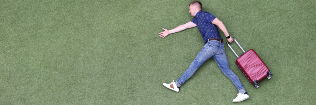 Young man with suitcase walking on green grass top view