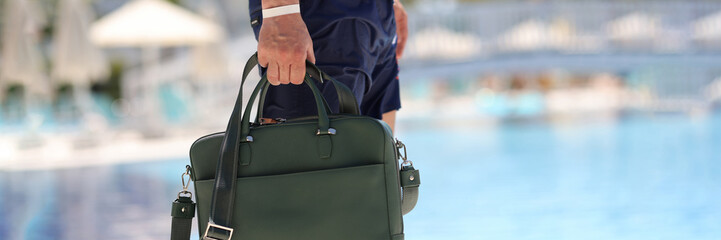 Man with bag for documents walking along edge of swimming pool closeup