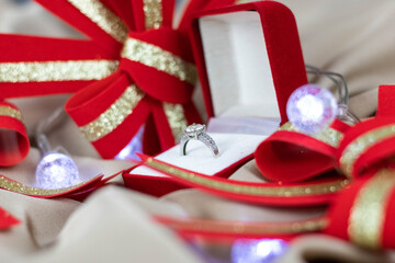 Selective focus of a diamond ring in a red jewelry box surrounded by decorative ribbons and bows