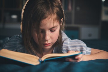 cute girl reading a book at home, lying on the bed. home pastime