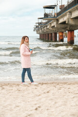 girl walking along the seashore. brunette drinks coffee. girl in a pink coat.