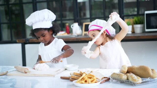 Diverse group of African American and Caucasian girls prepare the dough and bake cookies in the kitchen while learning in the class at school