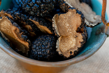 Truffles of Saint John in a small copper bucket. Sliced mushrooms. Black raw champignons on the surface. Top view. Dark background. Shallow depth of field.The artistic intend and the filters.