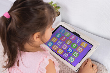 Preschooler Girl Playing Games Using Digital Tablet Lying On Sofa Alone. Curious Little Kid Girl Hold Pad Computer