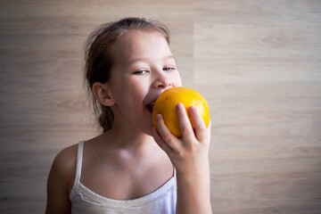 a little girl in a white t-shirt looks and shows orange citrus grapefruits shows how to eat them