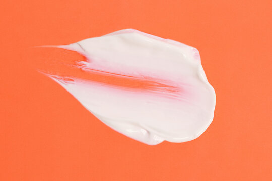 Abstract smear of white cosmetic cream on the orange background,abstract form.