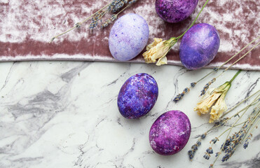 Purple Easter eggs on a textured background with dry flowers. A postcard with a place for text, top view.