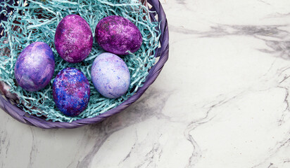 purple Easter eggs lie in a basket on a marble background. A postcard with a place for text.