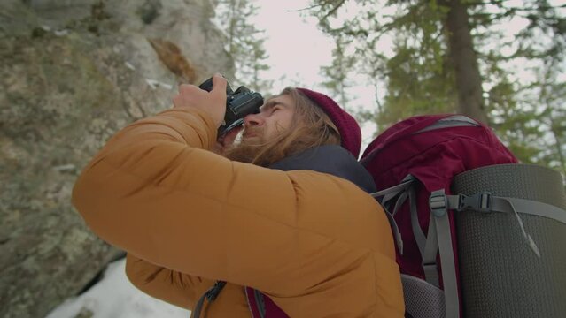 Low angle shot of male photographer taking pictures of mountains with professional camera during winter hike