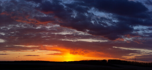 Panorama of sunset, blue clouds and red sun illuminates the clouds in gold.