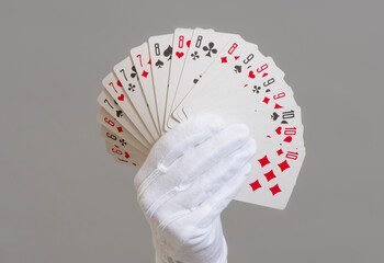 playing cards in a hand in a white glove on a gray background