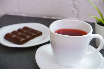 Sweet chocolate snack. White cup of tea close-up of a bar of chocolate in the background. World Chocolate Day and snack or breakfast concept.