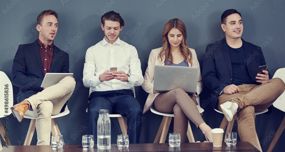 Poster On their wireless devices while waiting. Shot of a group of businesspeople using different wireless devices while waiting in line for an interview.