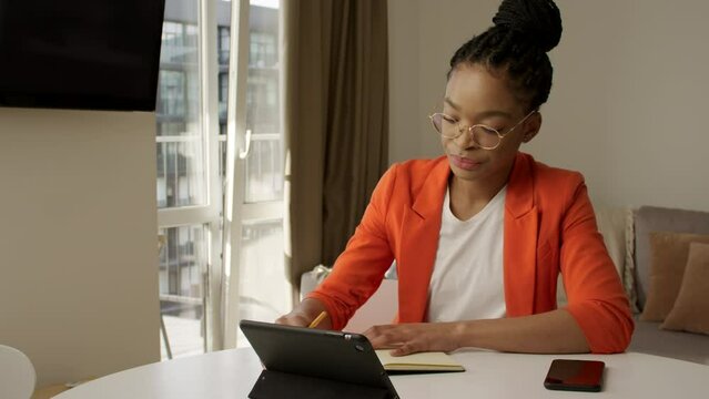 Young adult enterpreneur taking notes in her note pad in front of a tablet