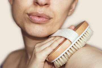 woman is using brush for dry massage. warm color, beige background. Dry body brush good for reduce...
