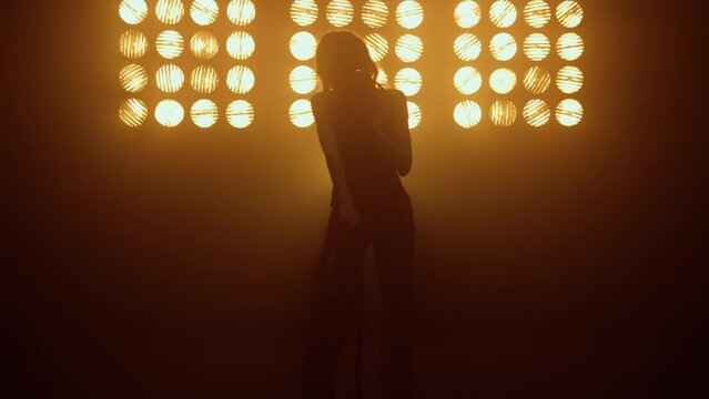 Silhouette singing woman dancing sensually near microphone at studio lights. 