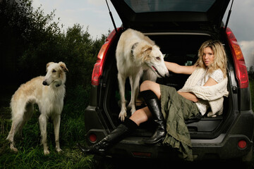 Young huntress before the hunt with two grayhounds in the black car