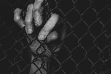 Old female hands hold on to a rusty fence in the dark, Ukrainian prisoners in the war in Ukraine,...