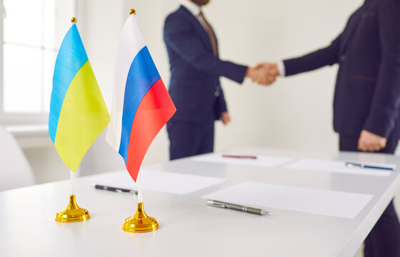 Russian Federation and Ukraine state representatives exchange handshakes over negotiation table with national flags. Successful diplomacy, signing peace treaty, ending conflict, stopping war concept