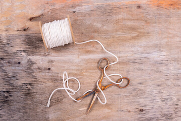 old rusty scissors tangled on a spool of thread against a background of wood texture
