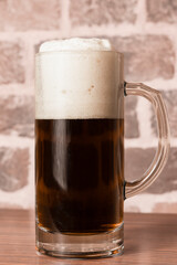 glass mug with dark foamy beer on a wooden table against a brick wall background