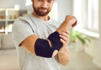 Unhealthy young man with arm sling on broken hand have rehabilitation at home. Unwell sick guy have...