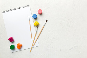 Album pages and paints, pencils, brush on a colored background. Top view with empty space. workplace for creativity. home teaching concept drawing