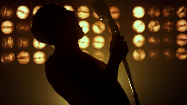 Singer performing song firely on stage closeup. Silhouette unknown man performer