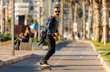 latin senior man with beard skateboard on bikeway in La Serena