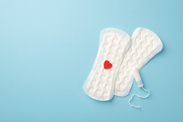 Top view photo of two panty liners with red heart and tampon on isolated pastel blue background with copyspace