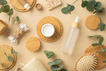 Eco cosmetics concept. Top view photo of bottles cream jar soap hair brush eucalyptus cotton buds and wooden stands on isolated beige background
