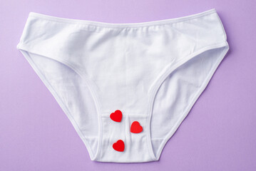 Top view photo of white cotton classic panties with red hearts on isolated pastel lilac background