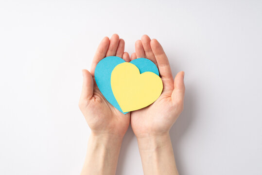Stop the war in Ukraine concept. Top overhead view photo of woman's hands demonstrating two yellow and blue hearts on palms on white background