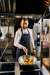Сhef in the professional kitchen with a frying pan and a fire..Chef's hands hold iron Pan and preparing food on cooker.