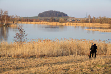 Para młodych ludzi z psem na spacerze brzegiem jeziora.	
