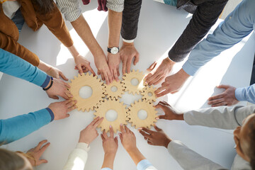 Top view close up of multiracial diverse businesspeople connect cogwheels work together for shared...
