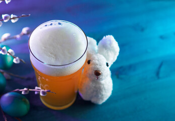 A glass of craft limited beer for the Easter holiday. White crocheted bunny . Copy space blue background