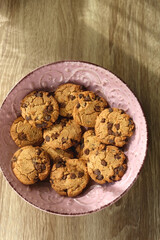 Pink plate filled with chocolate chip cookies on wooden table. Flat lay.