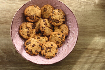 Pink plate filled with chocolate chip cookies on wooden table. Flat lay.