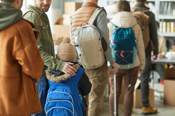 Back view at group of Caucasian refugees in line at donation center, focus on young child with...