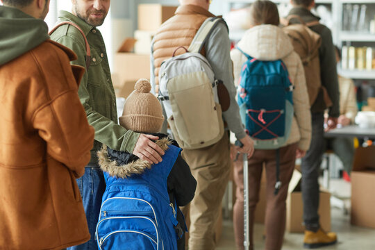 Back view at group of Caucasian refugees in line at donation center, focus on young child with backpack, copy space